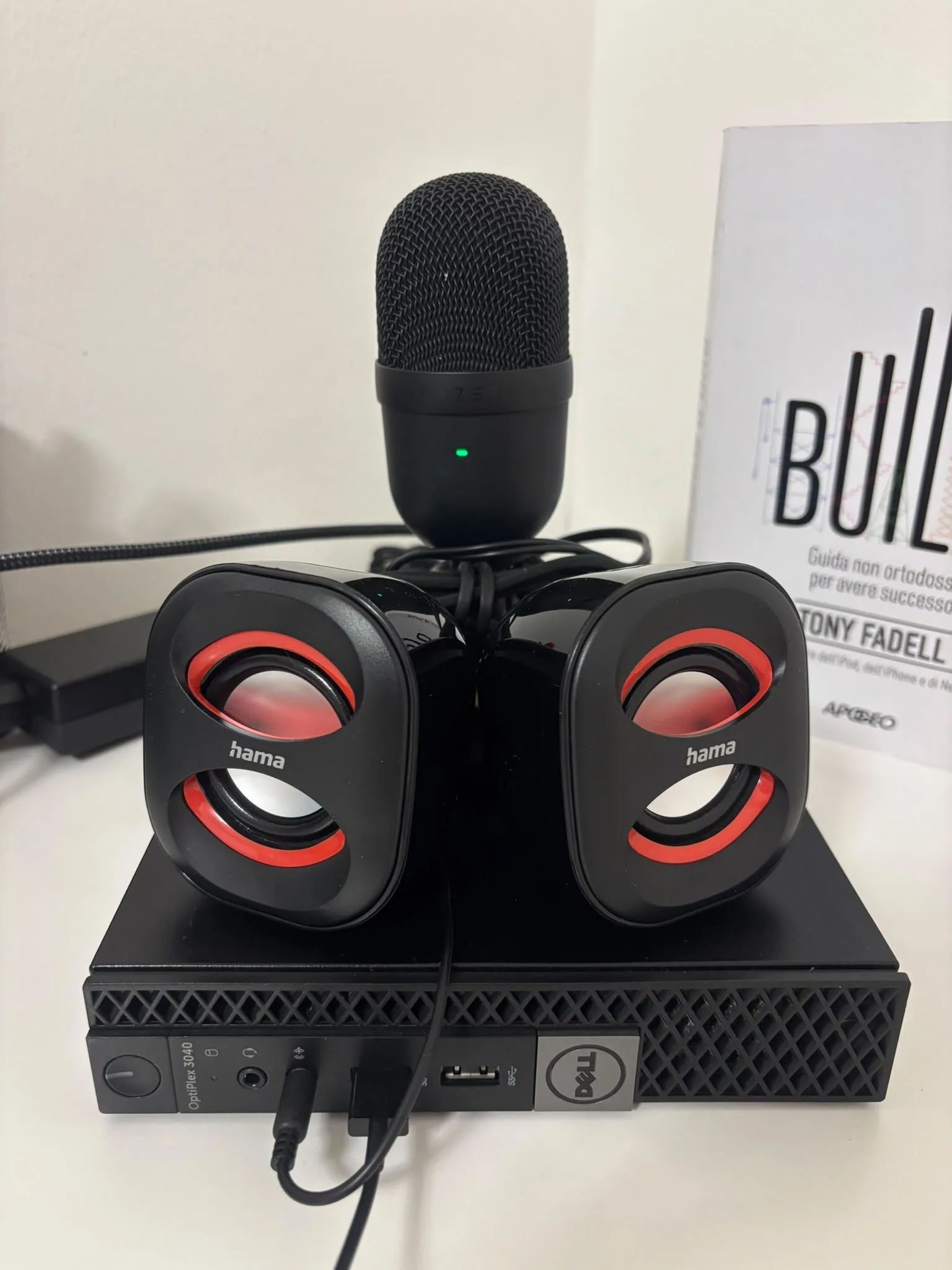 Franco: a small black Dell OptiPlex 3040, two round black and red Hama speakers sitting on top of it, and a black USB microphone standing behind, on a white desk.